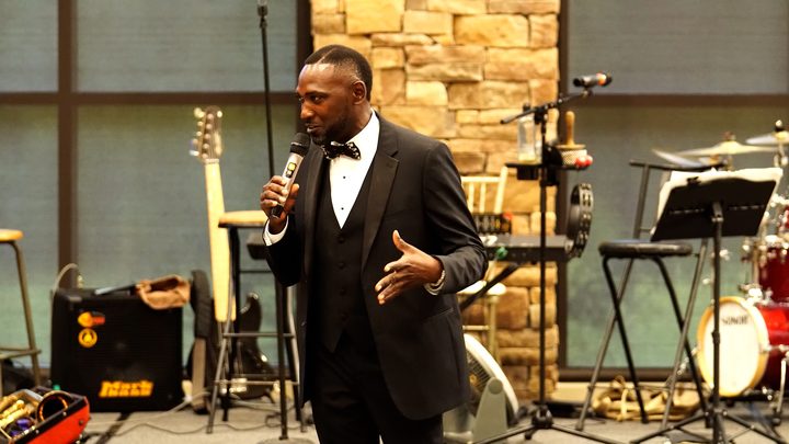 A speaker in a tuxedo addressing the room