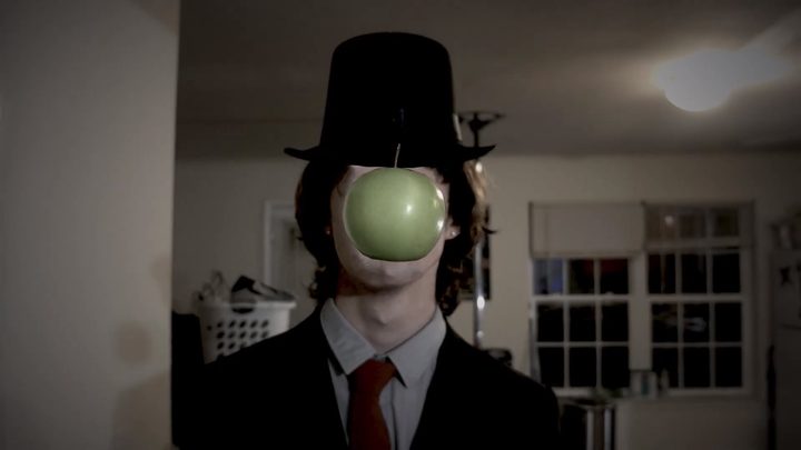 A bowler-hatted figure with a green apple over his face