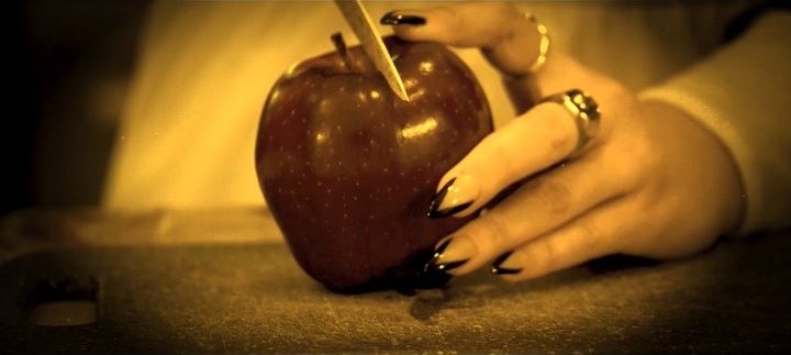 A hand pressing a straw into a red apple