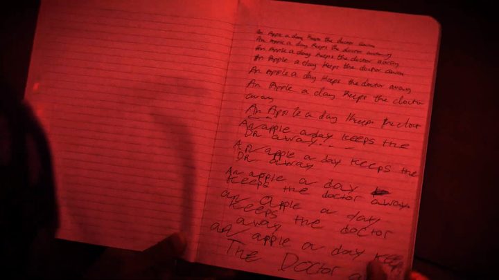 A handwritten notebook page under red light